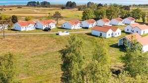 Un ensemble de maisons blanches aux toits rouges, disposées en rangée, se dressant sur un paysage côtier verdoyant, avec des arbres et une vue sur la mer.