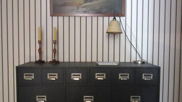 A black filing cabinet with multiple drawers against a striped wall, a framed landscape painting above it, a candle, and a desk lamp.