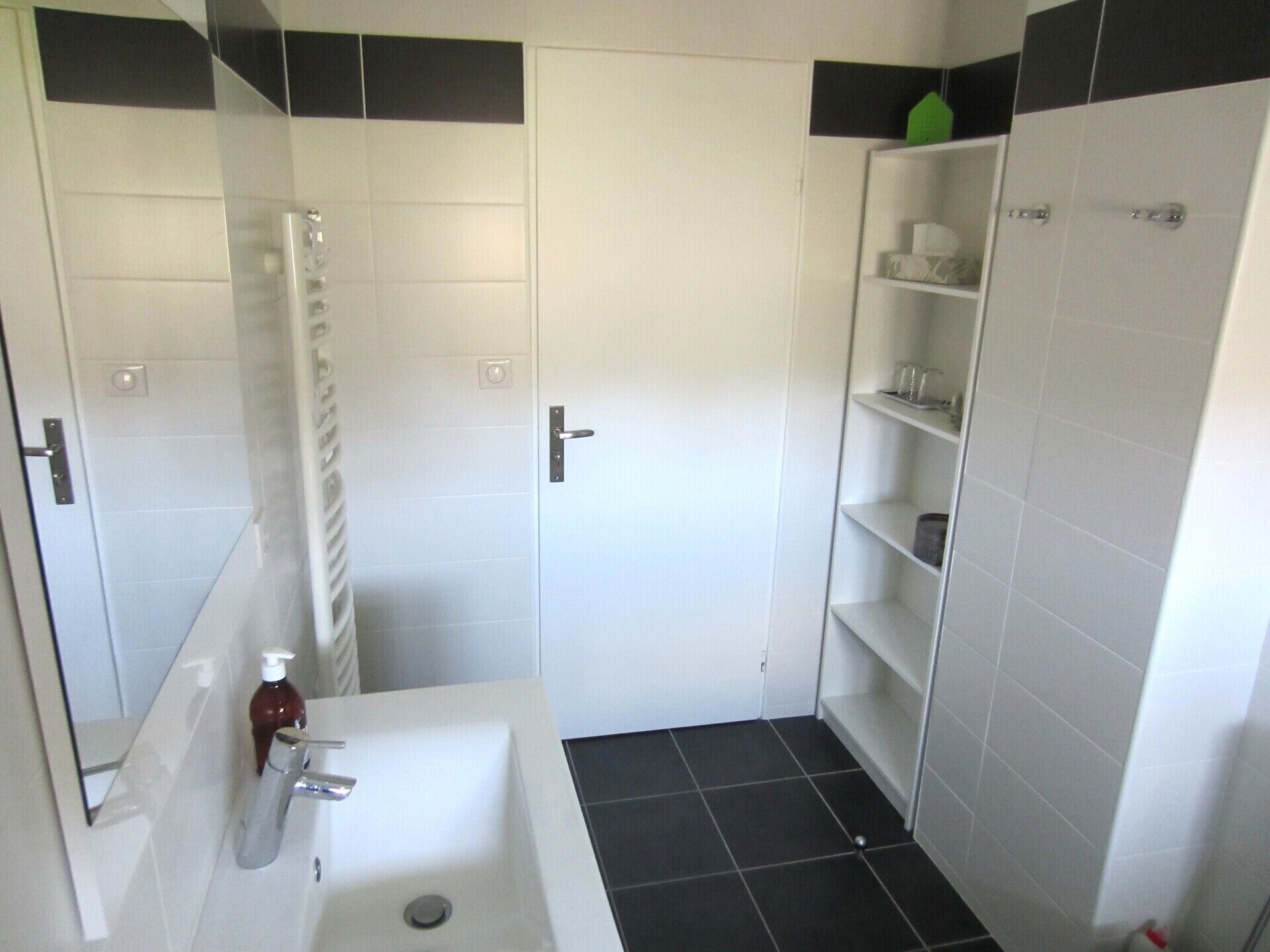 Un baño con lavamanos blanco, un espejo, toallero y zona de ducha.