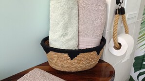 A bathroom with a wooden vanity, a woven basket holding rolled towels, and a toilet paper holder. - P'tit ranch SPA PRIVATIF Ô Rêves Atypiques (Boucé)