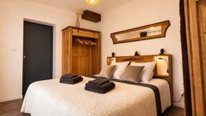 A bedroom with a bed, a wooden wardrobe, a mirror, and a door.