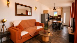 A living room with a sofa, a round wooden coffee table, a mirror, and a kitchen in the background.