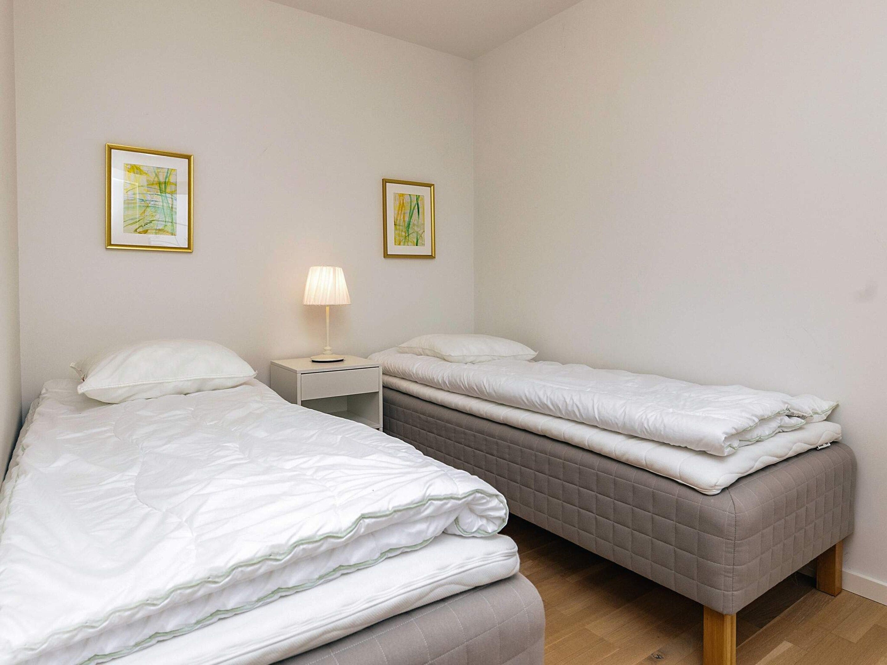 A bedroom with two beds, a bedside table with a lamp, and two framed pictures on the wall.