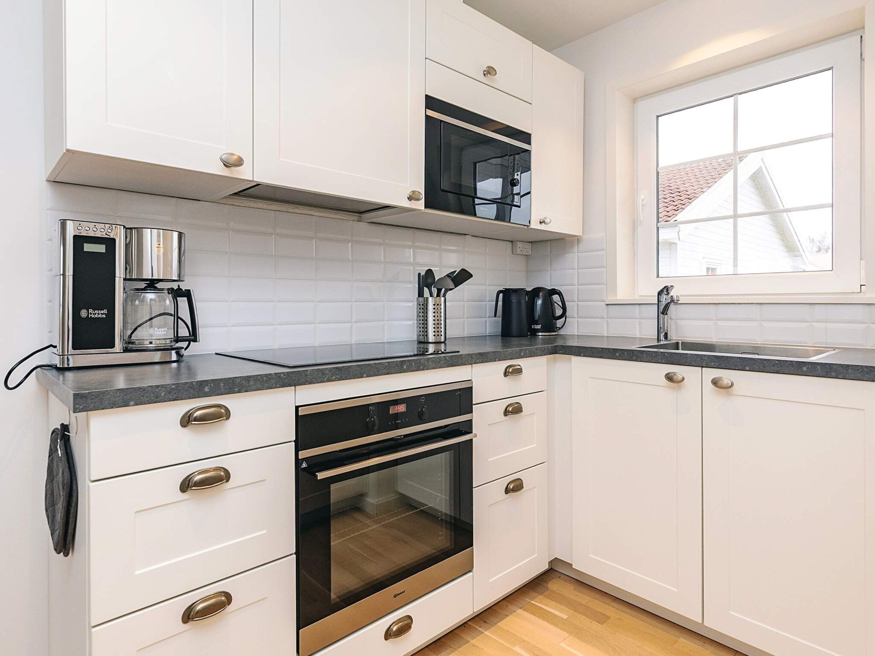 A modern kitchen with white cabinets, a built-in oven, a microwave, and a coffee maker.
