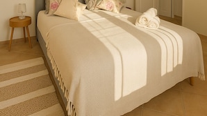 Une chambre à coucher avec un lit, des oreillers, une table de chevet, une lampe et une porte.