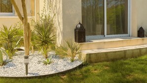 Une maison moderne dotée d’une grande porte-fenêtre coulissante, d’un petit jardin agrémenté de galets blancs et de plantes, et d’un arbre au premier plan.
