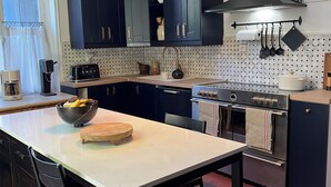 Una cucina moderna con mobili blu scuro, un piano cottura in acciaio inossidabile e un ripiano in marmo bianco.