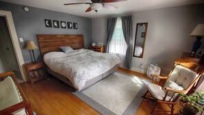 Ein Schlafzimmer mit einem hölzernen Bett, einem Nachttisch, einem Sessel, einem Ventilator und einem Spiegel.