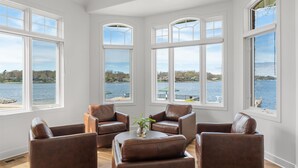 Een kamer met uitzicht op een meer, met een zithoek met leren stoelen en een bijzettafeltje.