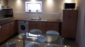 Une petite cuisine équipée d’un lave-linge, d’un évier, d’une fenêtre avec une plante et d’un four à micro-ondes posé sur un meuble.