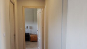Un couloir étroit, dont le sol est recouvert de moquette, mène à une pièce où se trouvent une commode en bois et une lampe.