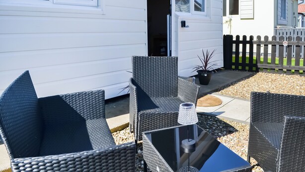 A mobile home with a patio area featuring wicker furniture and a small table with a lamp.