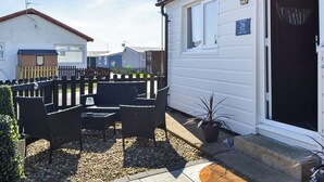 A caravan with a black door, a small outdoor seating area with chairs and a table, and a sign indicating the number 26.