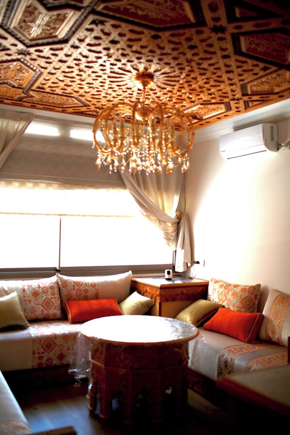 A room with a patterned ceiling, a chandelier, a sofa with patterned cushions, and a small round table.