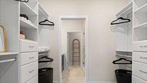 Un vestidor estrecho con estanterías blancas, perchas negras y una escalera de madera al fondo.