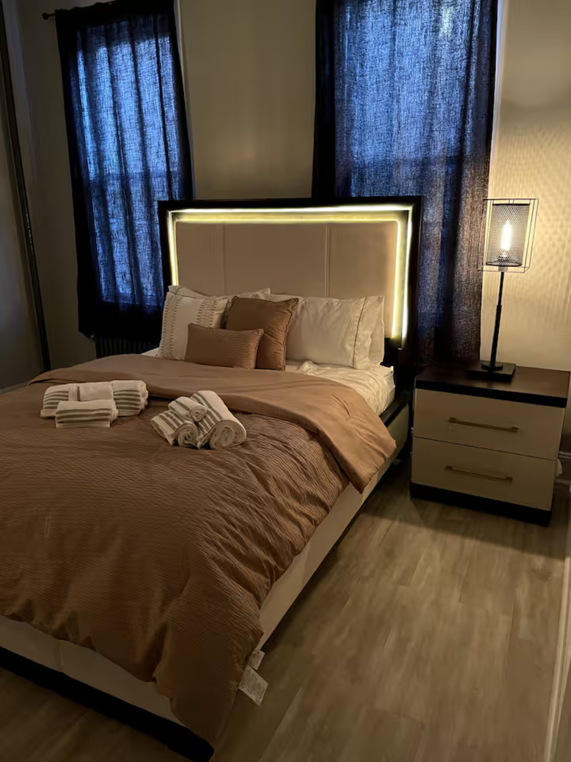 A neatly made bed with a headboard, a bedside table with drawers, and a floor lamp.