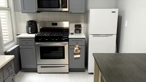 Una cocina compacta con gabinetes grises, estufa de acero inoxidable, microondas y refrigerador blanco.