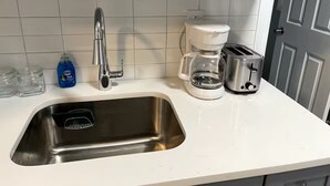 Una cocina con un lavamanos de acero inoxidable, una cafetera y un tostador.