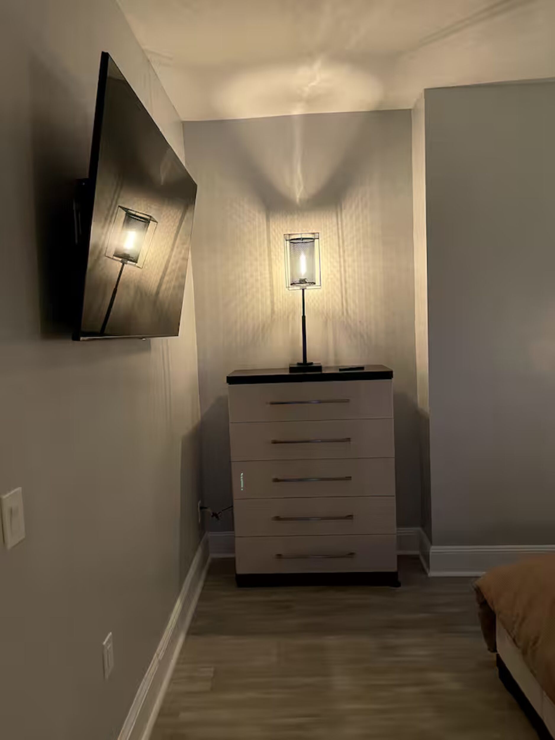 A bedroom with a bed, a dresser, a TV mounted on the wall, and a floor lamp.