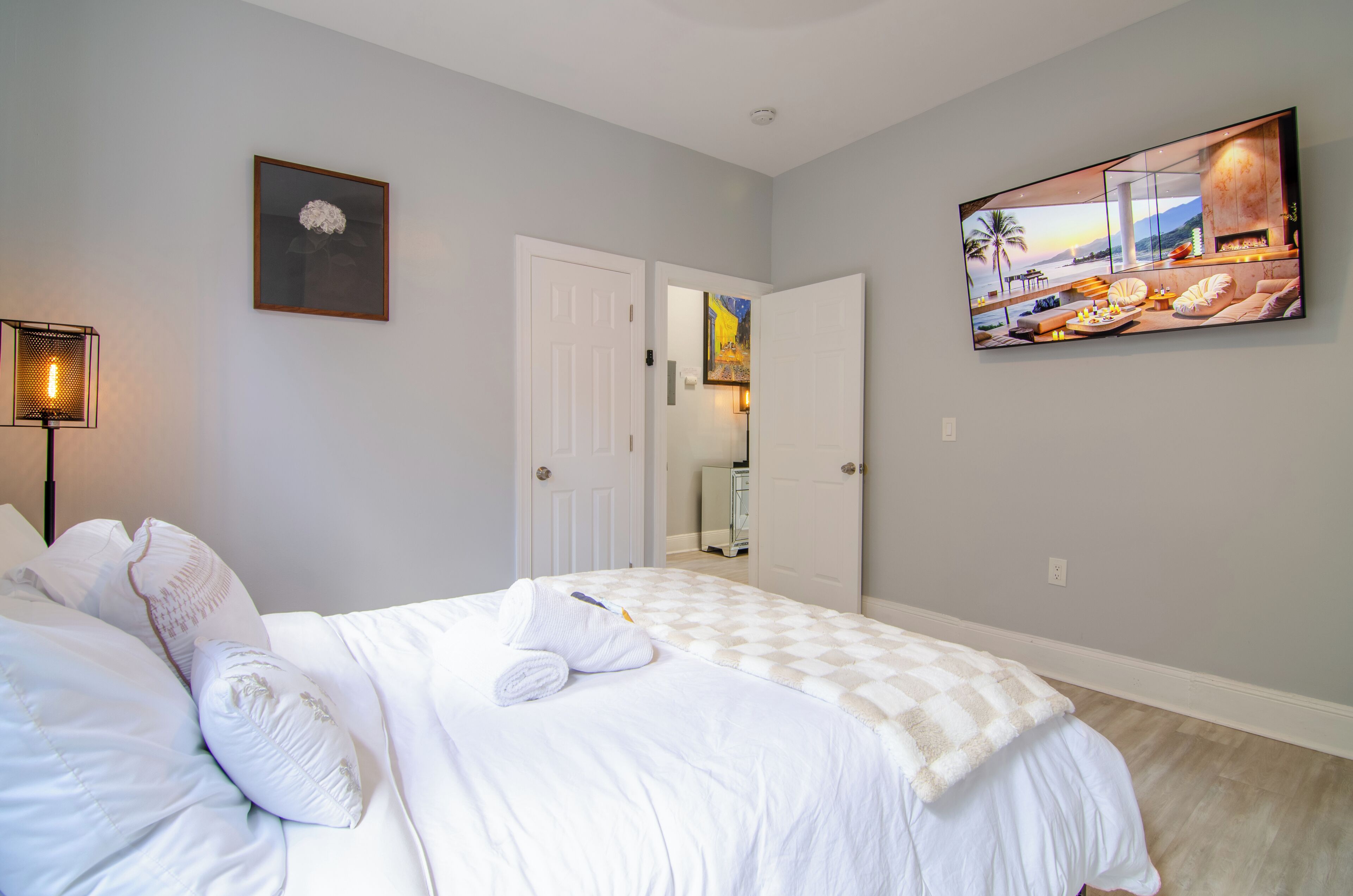 A hotel room with a bed, a painting, and a door leading to another room.