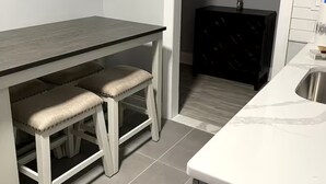 Una cocina con encimera blanca, mesa de madera oscura y dos taburetes.