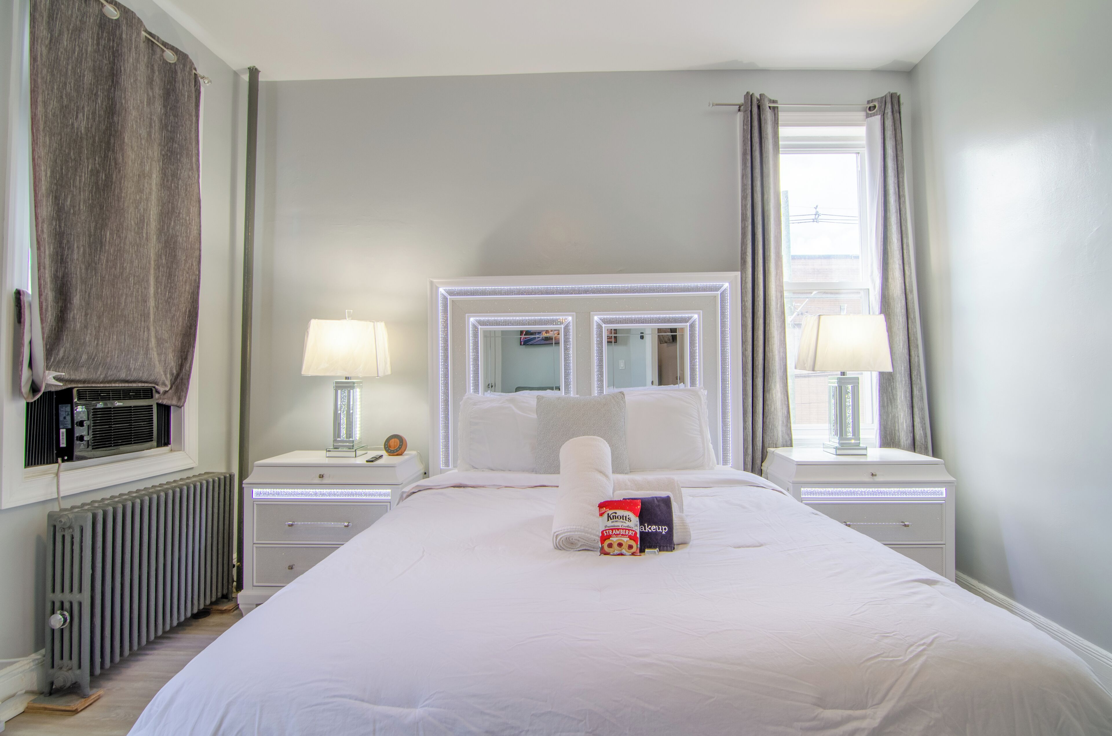 Een hotelkamer met een groot bed, twee nachtkastjes met lampen, een radiator en een raam met gordijnen.