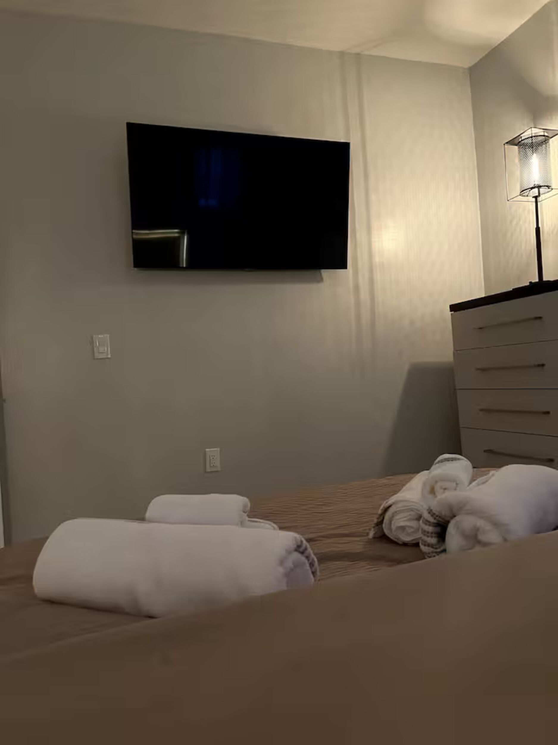 Una habitación de hotel con cama, televisión montada en la pared y cómoda.