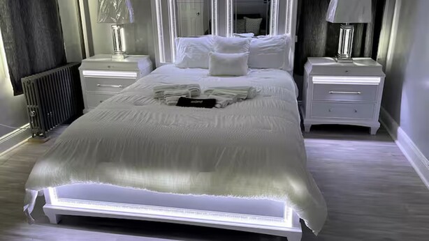 Un dormitorio moderno con una cama grande, mesitas de noche blancas y un espejo sobre la cama.