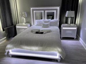 A modern bedroom with a large bed, white nightstands, and a mirror above the bed. - WORLD CUP + minutes to NYC (Union City)