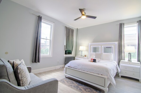 A bedroom with a bed, a nightstand, a bedside table, a ceiling fan, and a window with curtains. - WORLD CUP + minutes to NYC (Union City)