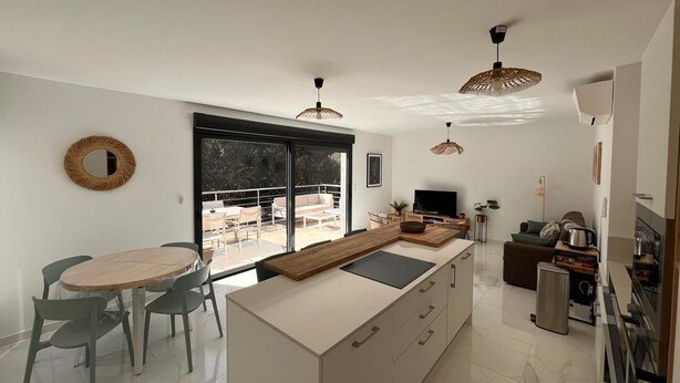 A modern kitchen with a dining area, large windows, and a view of the outdoors.