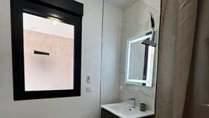 A modern bathroom with a glass shower enclosure, a white sink with a dark countertop, and a wicker shelf.