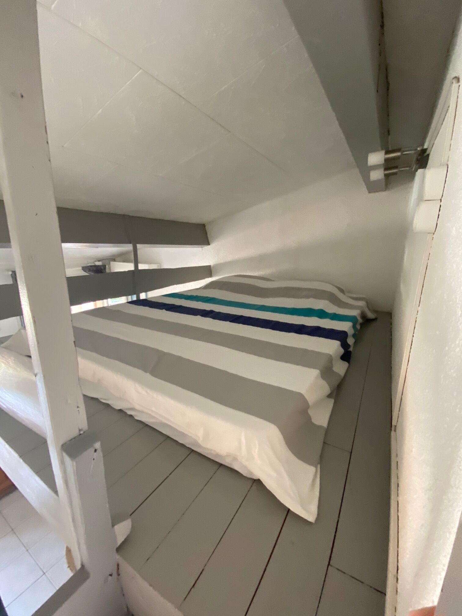A small, narrow room with a single bed, white walls, and a sloped ceiling.