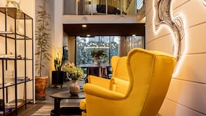 Un salon moderne avec un fauteuil jaune, une bibliothèque noire et une grande fenêtre donnant sur la ville.