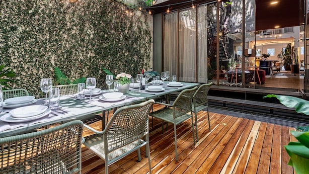 Un espace de restauration en plein air avec une table dressée pour quatre personnes, entourée de chaises en osier, le tout se détachant sur un mur de pierre recouvert de verdure.