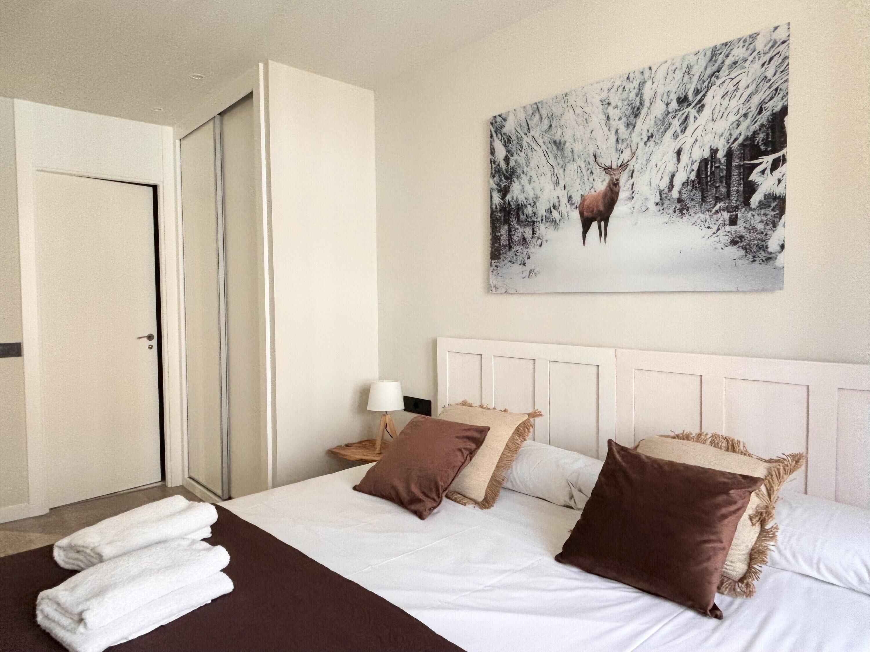 Habitación de hotel con cama, cabecera blanca y un cuadro de un ciervo en un bosque nevado.