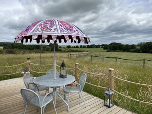 A wooden deck with a round table and chairs, an umbrella, and a lantern. - Cabins in Oxfordshire With Hot Tub & Meadow Views (Banbury)
