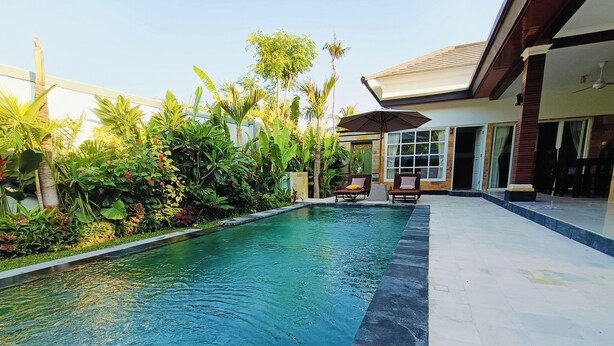 A swimming pool with a tiled edge, surrounded by lush greenery and a building with a tiled roof and windows. - 2BR Pool Villa-Twin Flower (Banjar)