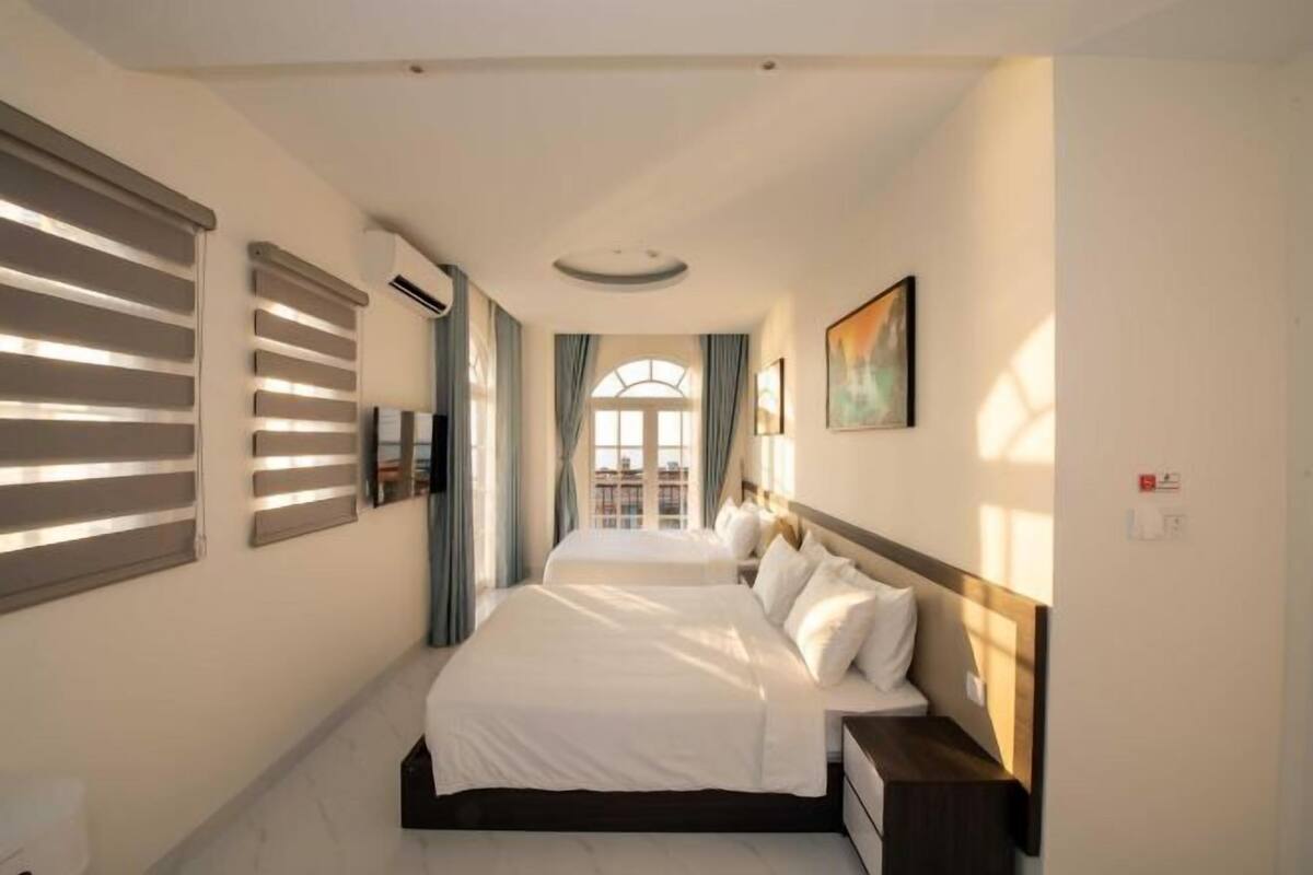 Une chambre d’hôtel avec deux lits, une vue sur le paysage urbain par la fenêtre et un tableau accroché au mur.