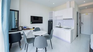 A modern kitchen with white cabinets, a black refrigerator, and a built-in oven. There is a dining area with a round table and grey chairs. - Hoàng Hôn Hotel (Phu Quoc)