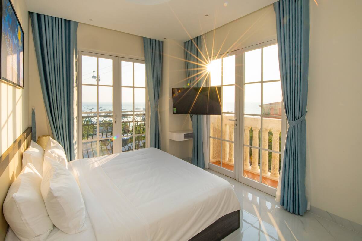 Une chambre d’hôtel avec un grand lit, un téléviseur fixé au mur et un balcon avec vue sur la mer.
