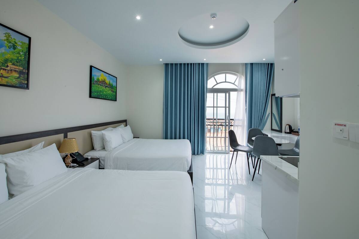 Une chambre d’hôtel avec deux lits, un bureau, une chaise et une grande fenêtre avec des rideaux.