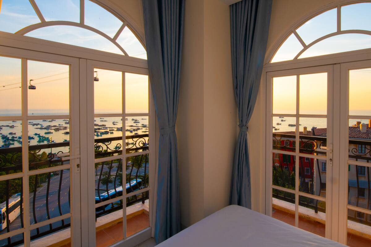 Un balcon avec un lit, des rideaux et une vue sur les bateaux et les bâtiments.
