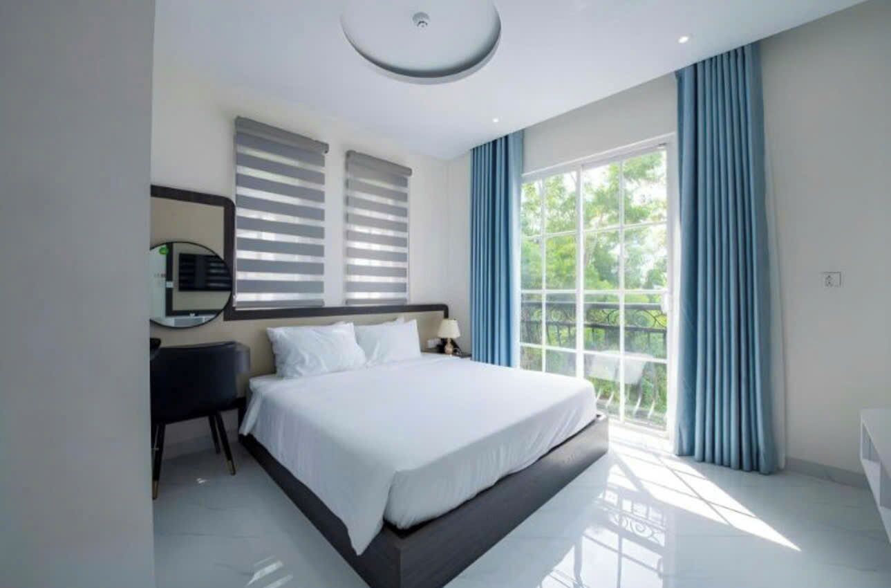 A modern bedroom with a large bed, a bedside table, a mirror, and a window with curtains.
