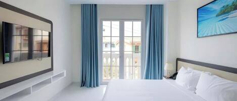 A hotel room with a large bed, a flat-screen TV mounted on the wall, and a balcony with blue curtains.