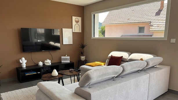 A modern living room with a large flat-screen TV, a sofa, a coffee table, and a window with a view of a building.