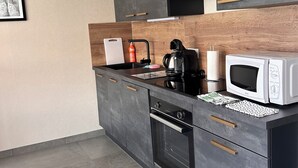 A modern kitchen with dark cabinetry, a microwave, a coffee maker, and a wooden backsplash.
