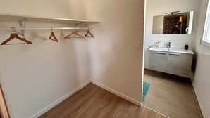 A small, modern room with a wooden floor, a white wall, and a built-in shelf with three wooden hangers.