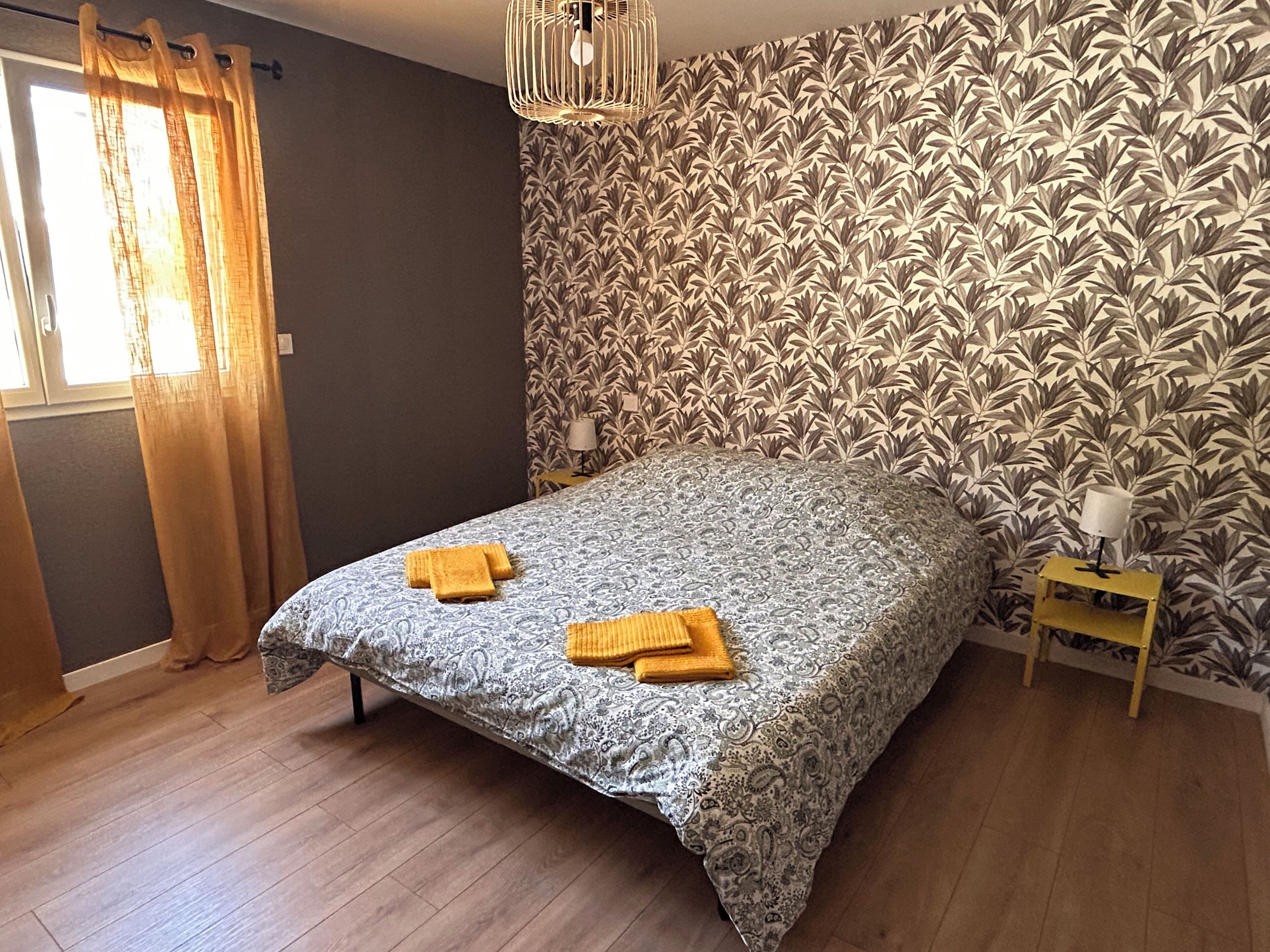 Ein Schlafzimmer mit einem Bett, zwei Nachttischlampen, einem Fenster mit Vorhängen und einer Wand mit Muster.
