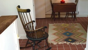 Ein Zimmer mit Schaukelstuhl, Tisch, gemustertem Teppich, Radiator und einem Poster an der Wand.